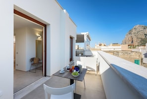 A balcony with a table set for breakfast, a chair, and a view of the sea and buildings. - IL MARE DENTRO SUITES (San Vito Lo Capo)