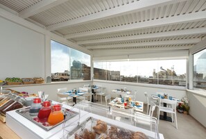A breakfast buffet with various food items and beverages, white furniture, and large windows offering city views. - IL MARE DENTRO SUITES (San Vito Lo Capo)