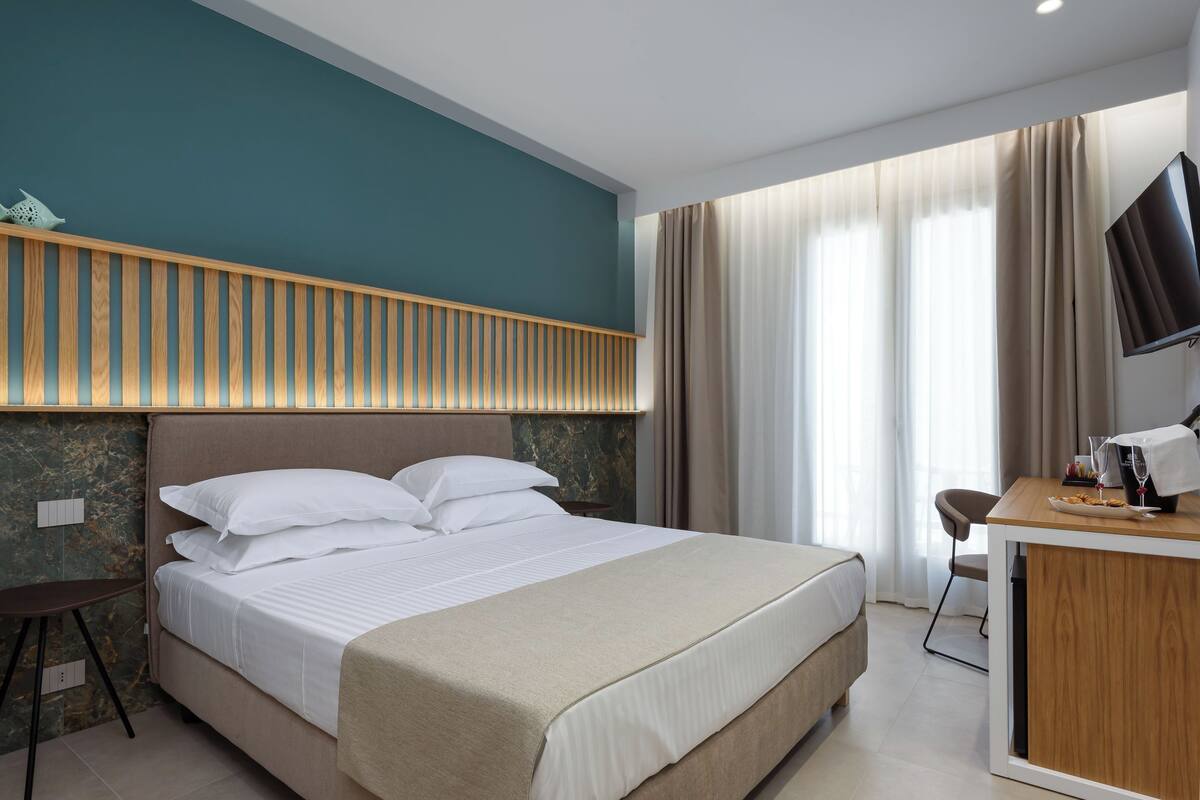 A hotel room with a large bed, a wooden headboard, a desk with a chair, and a TV.