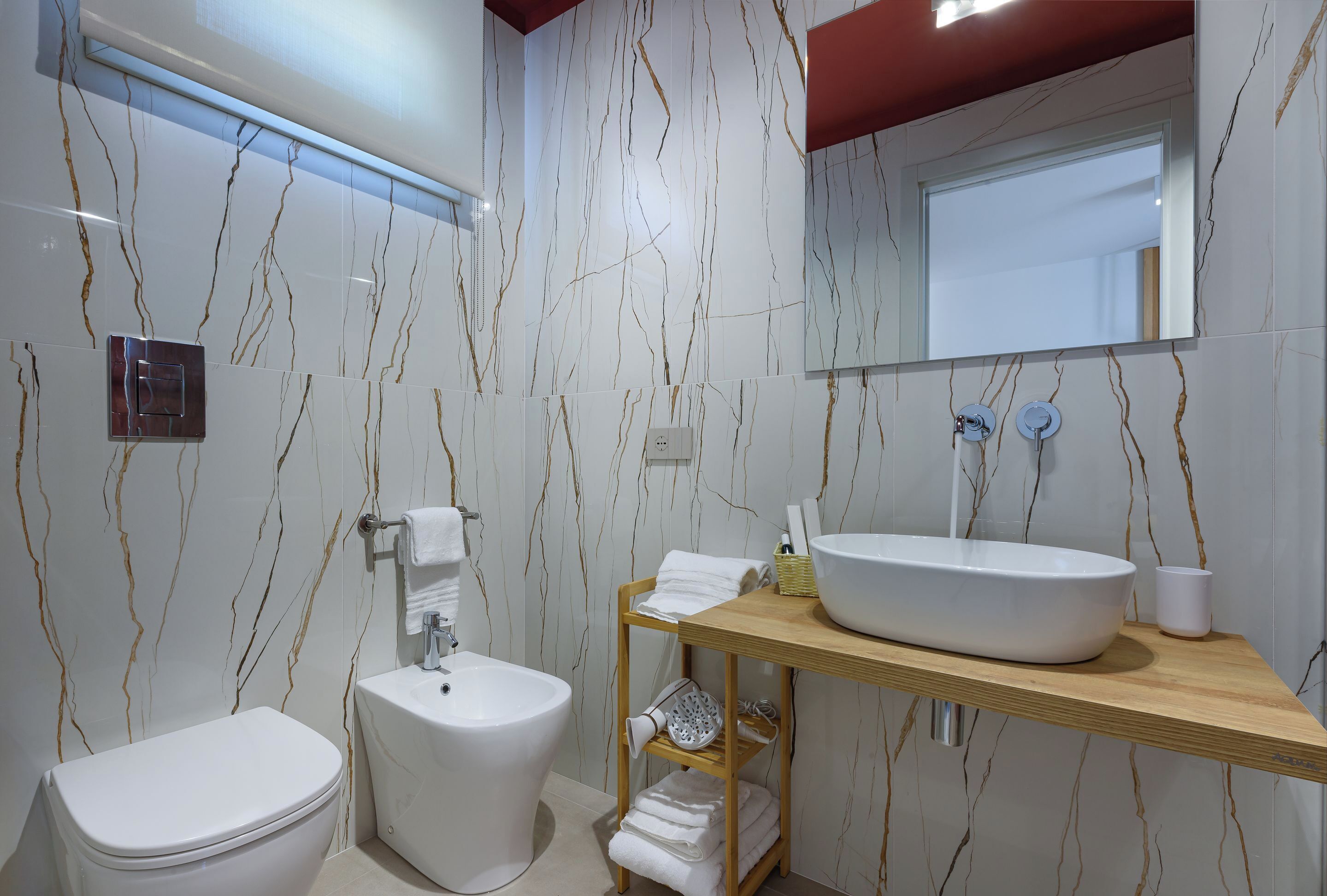 A modern bathroom with a white toilet, bidet, and a wooden vanity with a large sink and mirror.