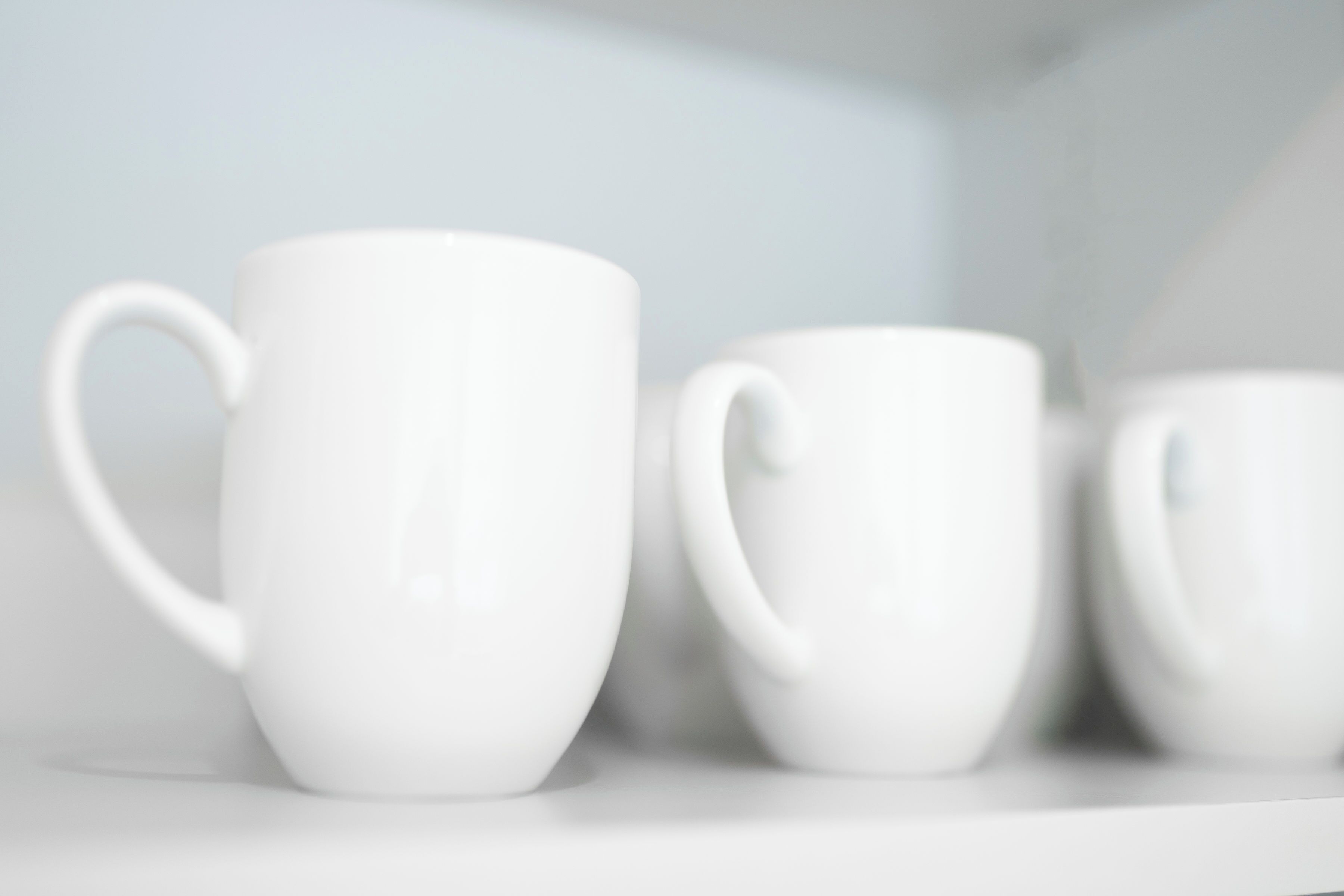 Three white ceramic mugs on a white shelf.