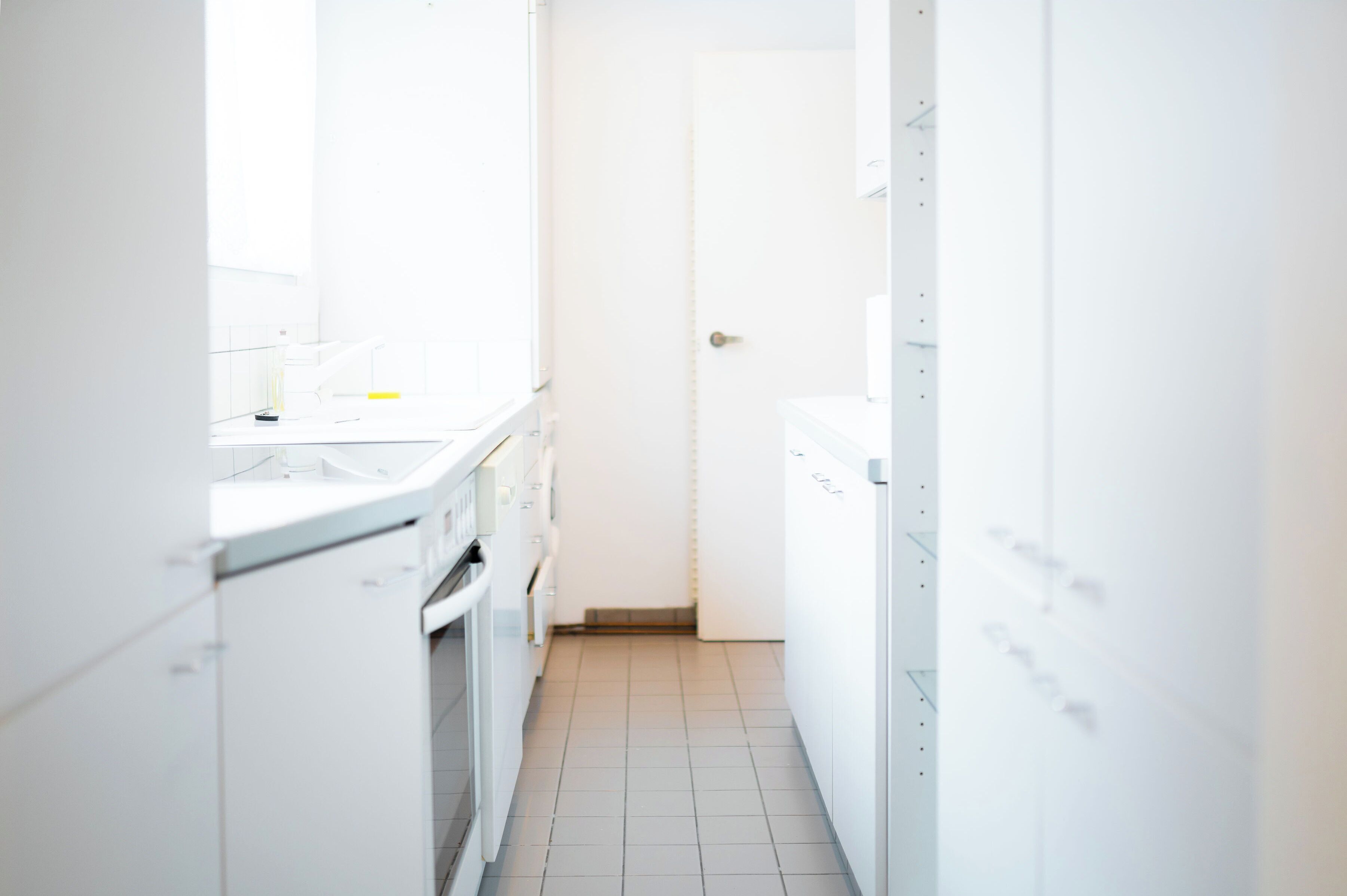A narrow, white kitchen with a door at the end, a countertop, and a stove.