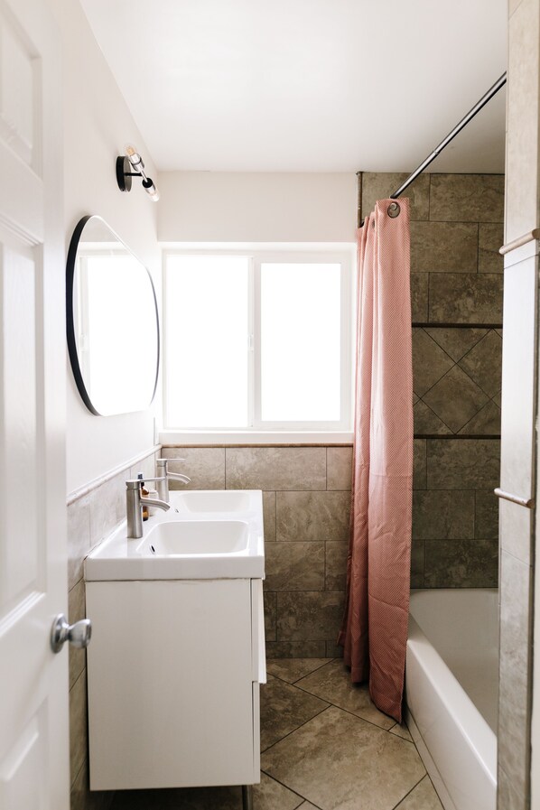 A bathroom with a white vanity, a mirror, a window, and a shower curtain.