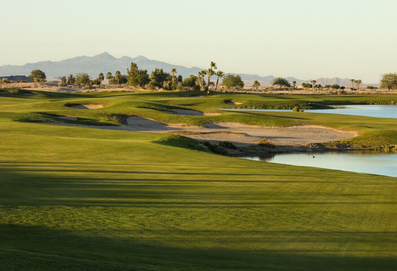 A golf course with sand bunkers, a water hazard, and palm trees.