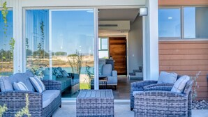 Un espace de vie extérieur moderne, avec des meubles en osier, une porte vitrée donnant sur un patio et une vue sur le paysage.