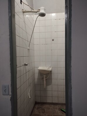 Un baño pequeño con azulejos, ducha, lavamanos e inodoro.