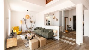Uma sala de estar espaçosa com piso de madeira, um sofá verde, uma poltrona amarela e uma escrivaninha de madeira.