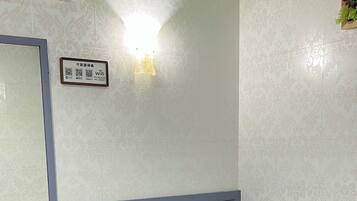 A hotel room with a bed, a bedside table with a lamp, a mirror, and a wall-mounted sign with QR codes.
