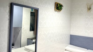 Une chambre d’hôtel avec un lit, un grand miroir, une petite plante et une salle de bain équipée d’un lavabo et de toilettes.