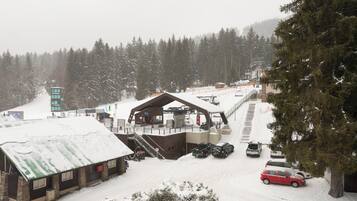 A snow-covered lodge with a ski lift, a parking area, and a forested backdrop.