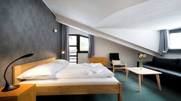 A modern hotel room with a wooden bed, a small desk, a sofa, and a view of the outdoors through a window.