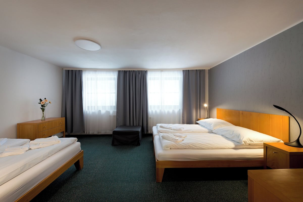 Une chambre d’hôtel avec deux lits, une table de chevet en bois, un bureau, une chaise et une fenêtre avec des rideaux.