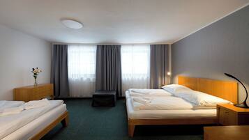 A hotel room with two beds, a wooden nightstand, a desk, a chair, and a window with curtains.