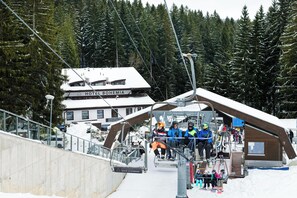 A ski lift with passengers, a hotel named "HOTEL BOHEMIA" in the background, and a snowy forested area.