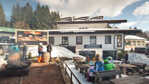 A restaurant with outdoor seating, a sign for 'Hotel Bohemia', and a snowy environment. - Hotel Bohemia (Zelezna Ruda)