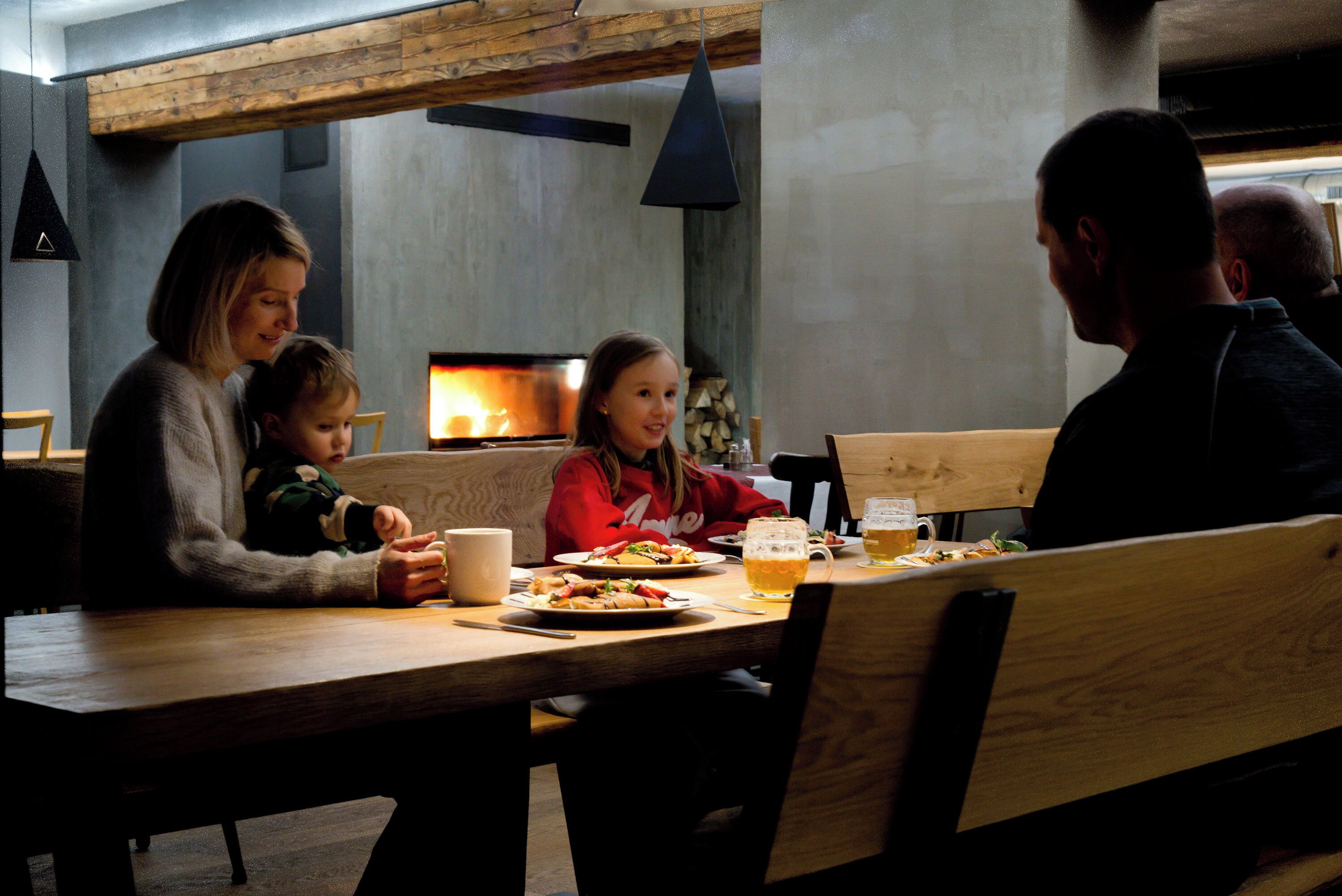 A family dining at a wooden table with a fireplace in the background.