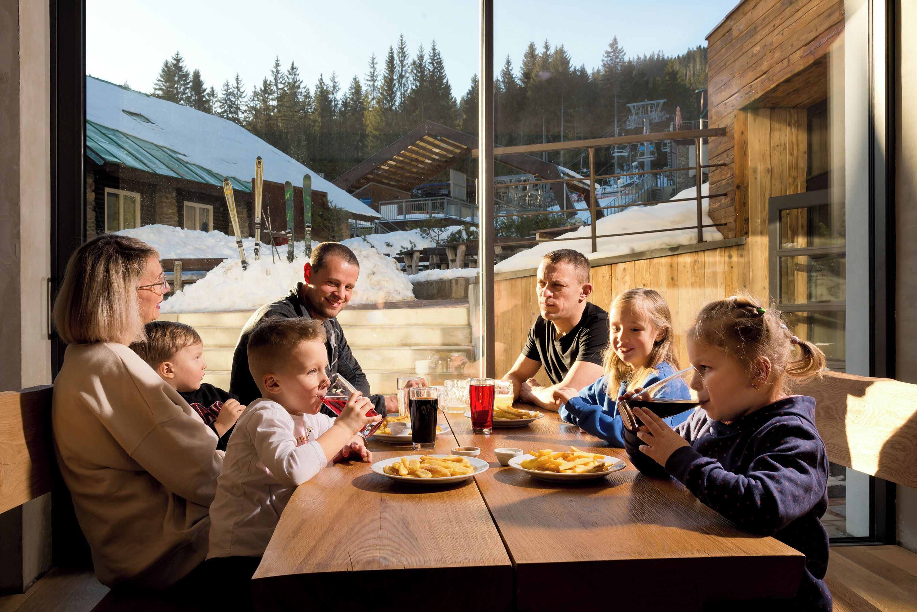 A family dining at a wooden table with a view of a ski resort.