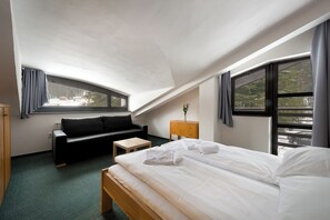 A modern hotel room with a bed, a sofa, a small table, and a nightstand. - Hotel Bohemia (Zelezna Ruda)