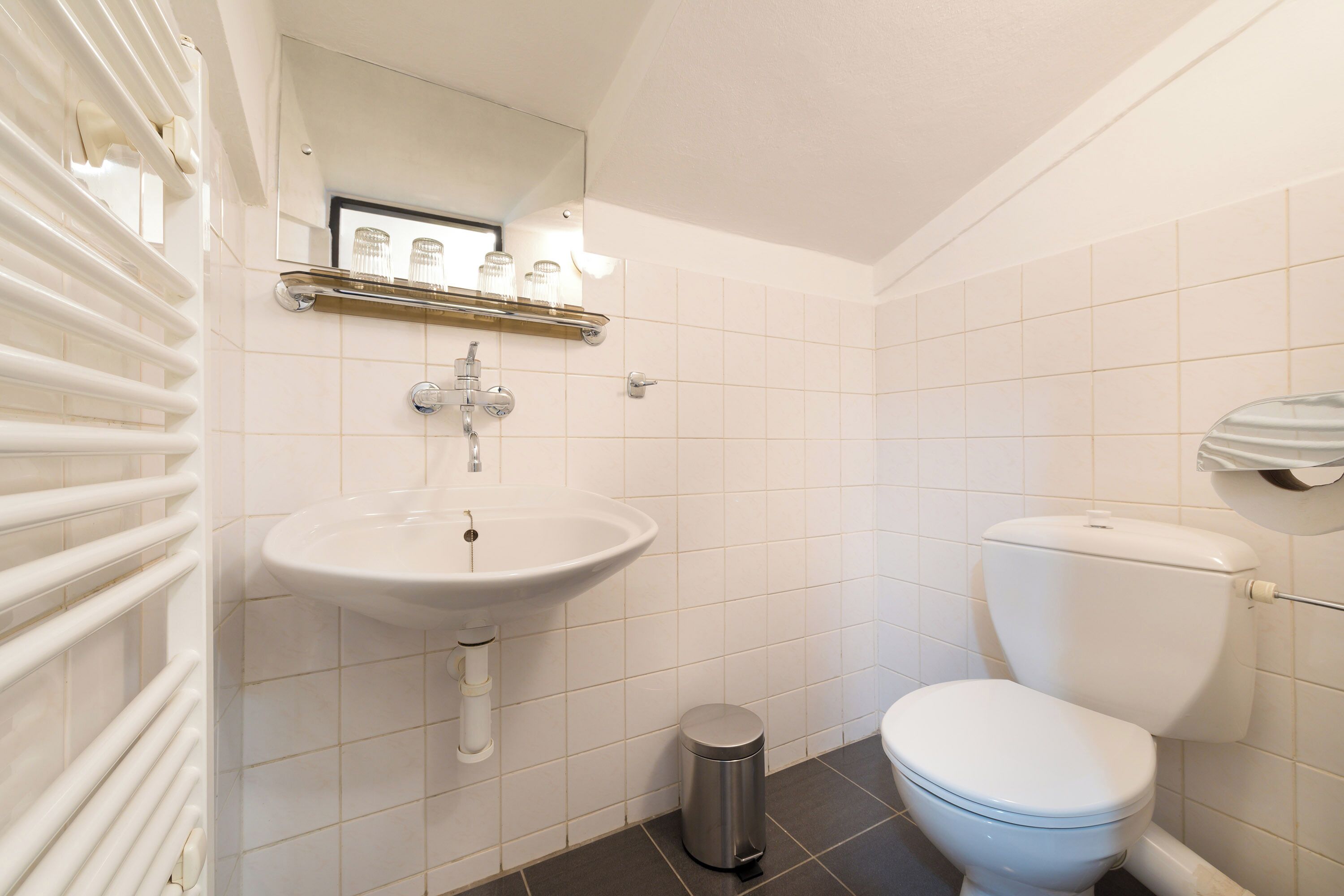 Et badeværelse med en hvid vask, toilet og skraldespand.
