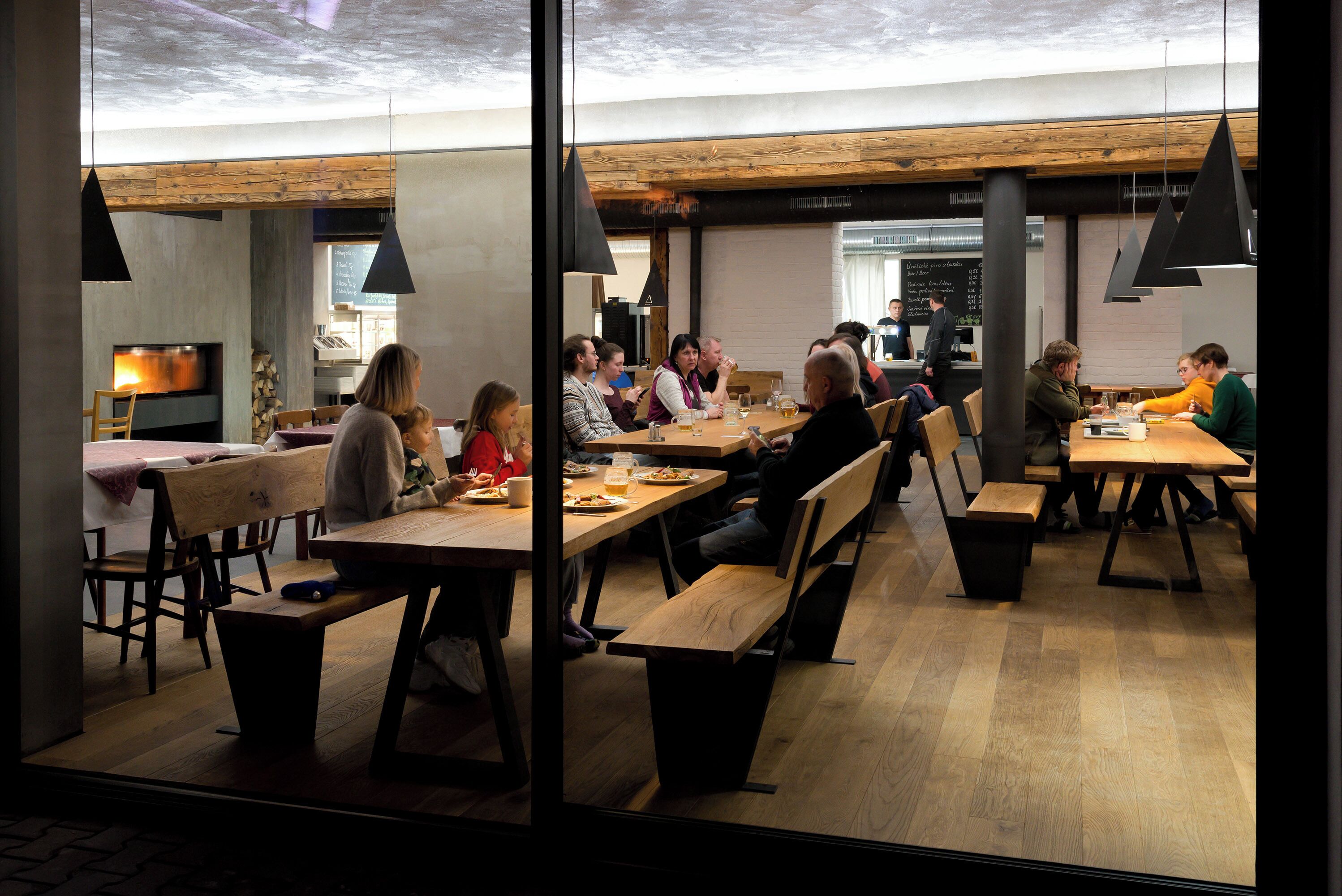 Uma sala de jantar moderna com mesas e bancos de madeira, lareira e luminárias pendentes.