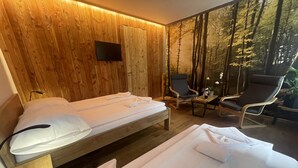 A room with a wooden wall, a bed with white linens, two chairs, a small table, and a TV mounted on the wall. - Hotel Bohemia (Zelezna Ruda)