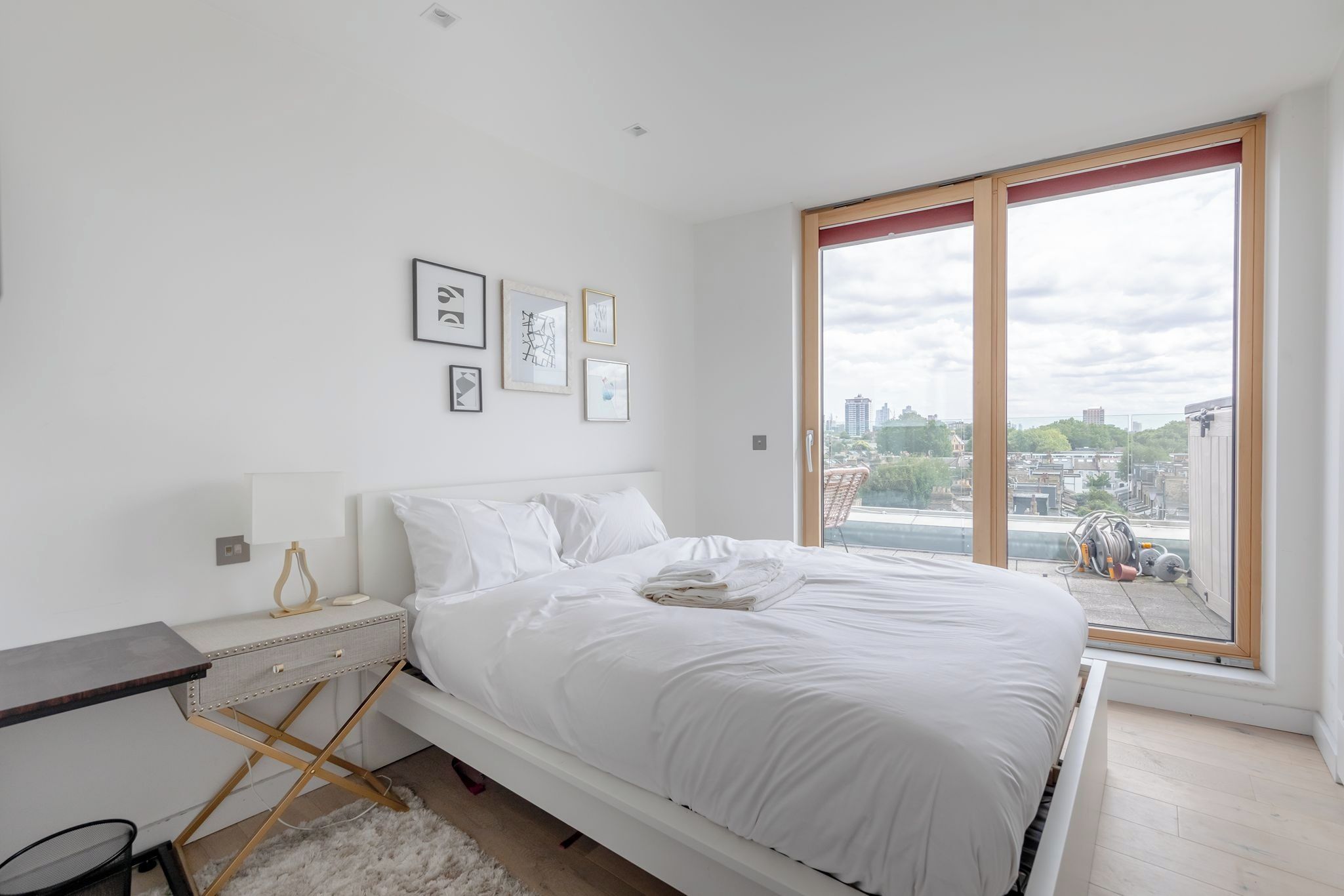 A bedroom with a large bed, a bedside table, a chair, and a window with a city view.