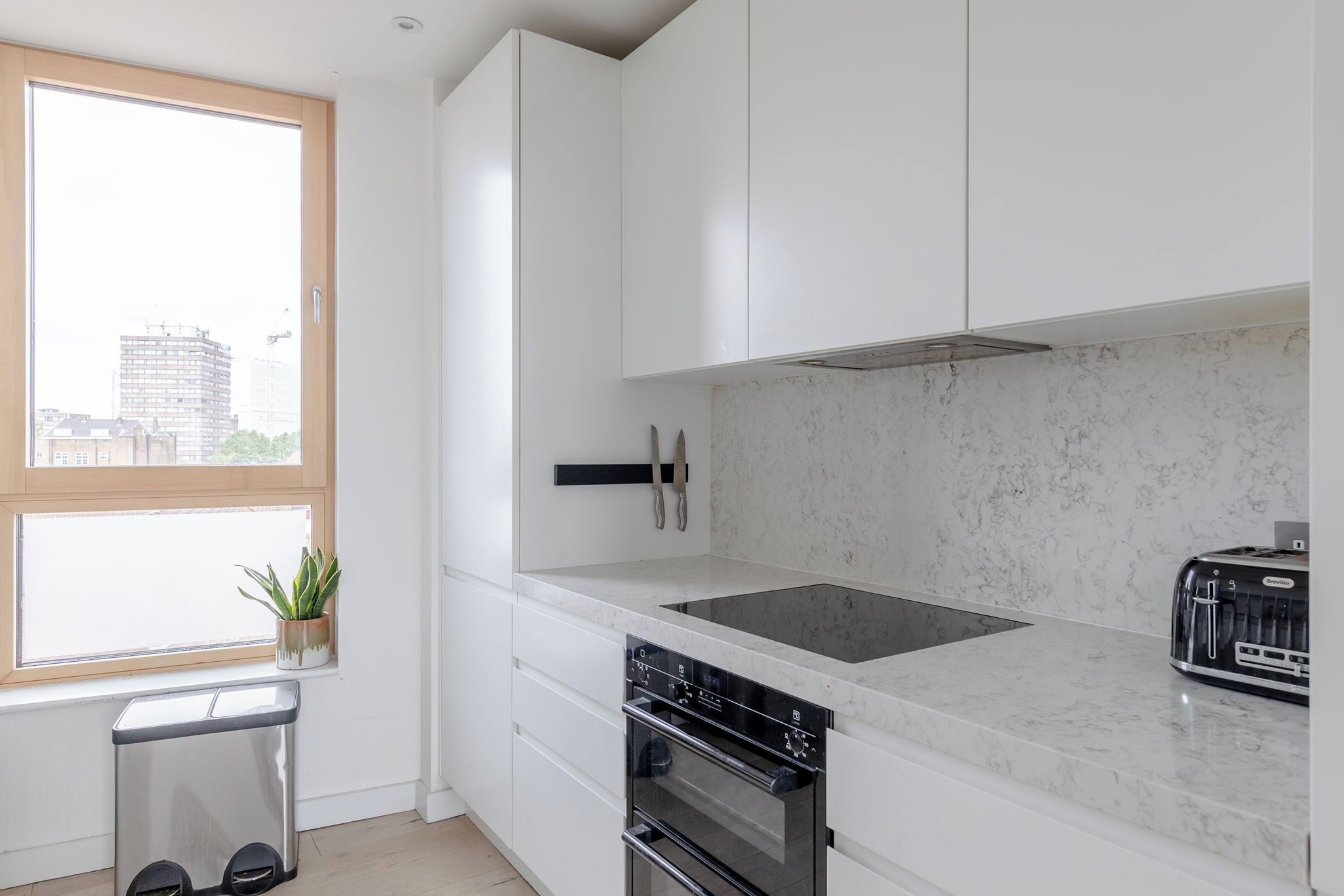 Una cucina moderna con mobili bianchi, forno integrato, piano cottura e una finestra con vista sugli edifici.