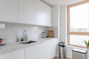 Une cuisine moderne avec des meubles blancs, un plan de travail en marbre, un évier en acier inoxydable, une machine à café et une poubelle.