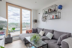 Un salon moderne avec un canapé gris, une table basse en verre et une grande fenêtre donnant sur la ville.