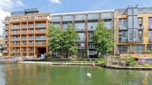 A modern apartment building with multiple balconies, a water body in front, and a small bridge. - Bright and Airy 2BD Flat in Haggerston (London)
