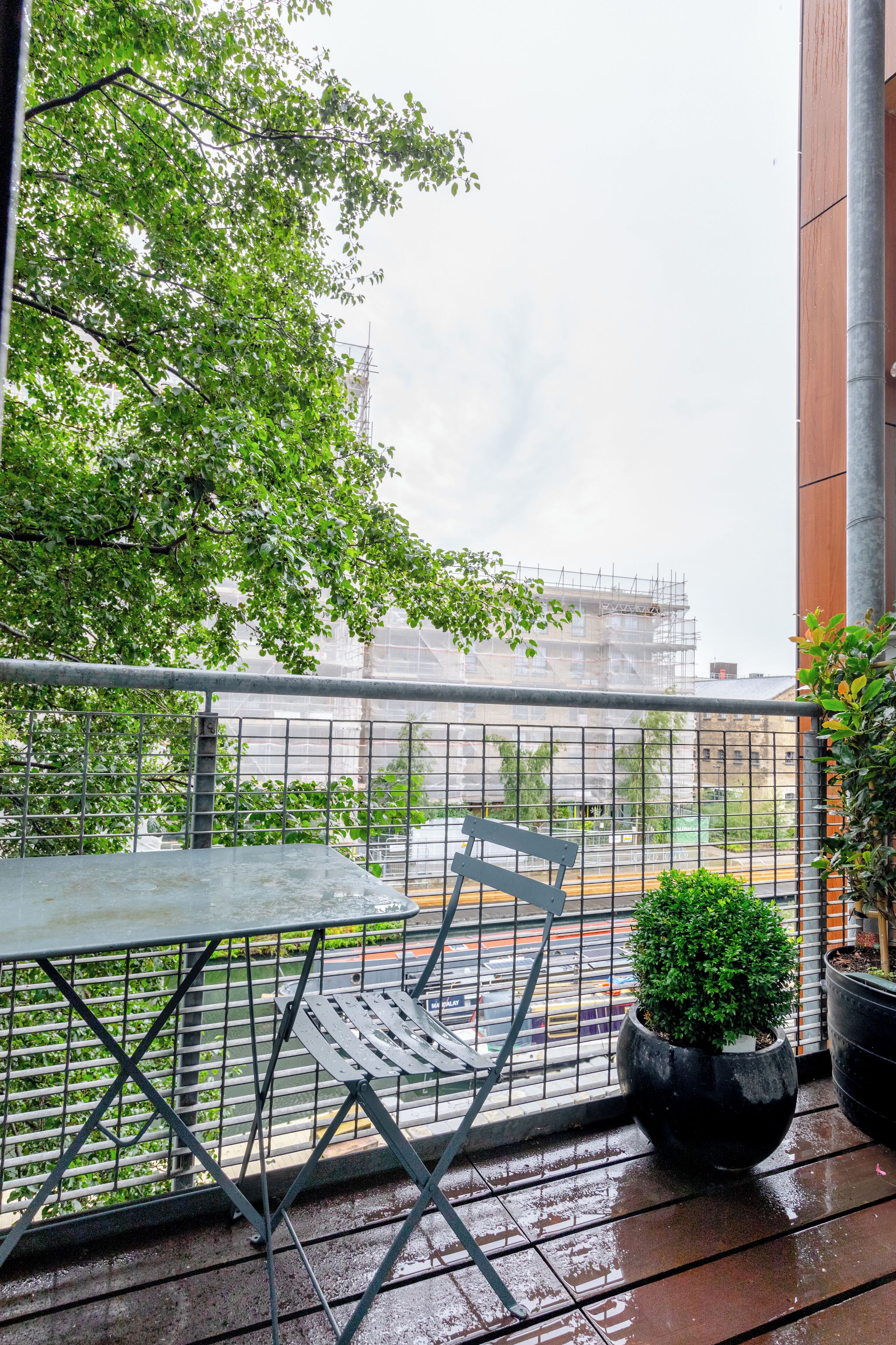 A balcony with a metal table and chair, a potted plant, and a view of a construction site.