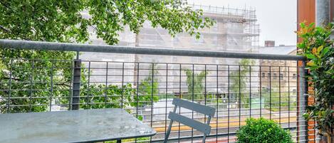 A balcony with a metal table and chair, a potted plant, and a view of a construction site.