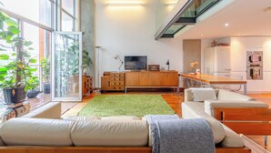 A modern living space with a large window, a green rug, a sofa, a dining table, and a kitchen area. - Bright and Airy 2BD Flat in Haggerston (London)