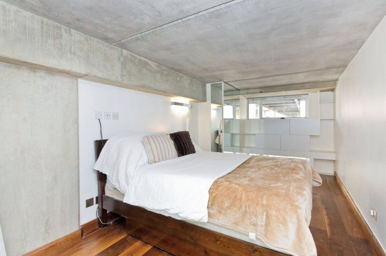 Een slaapkamer met een bed, houten vloeren en een betonnen plafond.
