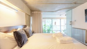 A hotel room with a large bed, a wooden headboard, and a view of the outdoors through a glass door. - Bright and Airy 2BD Flat in Haggerston (London)