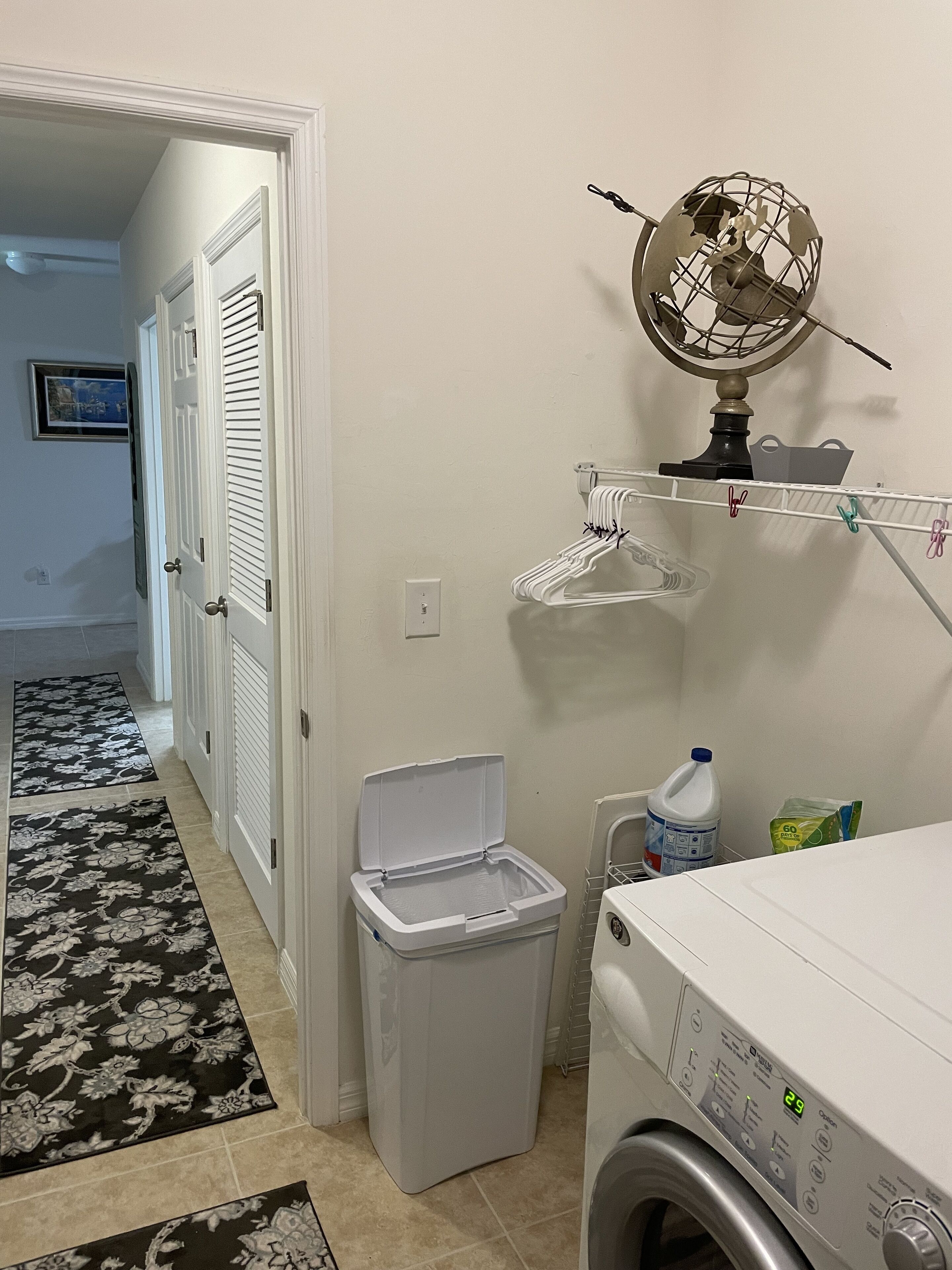 A laundry room with a washing machine, a drying rack, a trash bin, and a globe on a shelf.