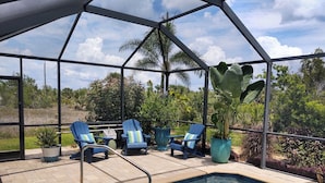 A covered outdoor swimming pool area with blue chairs and potted plants. - South Gulf Cove 4BR/2BA Heated Pool ,15 mins to the GULF (Port Charlotte)
