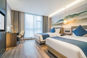 Hotellihuone, jossa on kaksi sänkyä, työpöytä, tuoli, televisio ja taulu, jossa on kuvattuna rantamaisema.