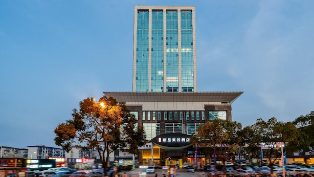A modern hotel building with a prominent glass facade, a flat roof, and a parking lot in front. - Rezen Dong Hotel (Shanghai)