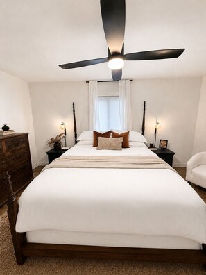 A bedroom with a bed, a ceiling fan, bedside tables, a dresser, and a chair.