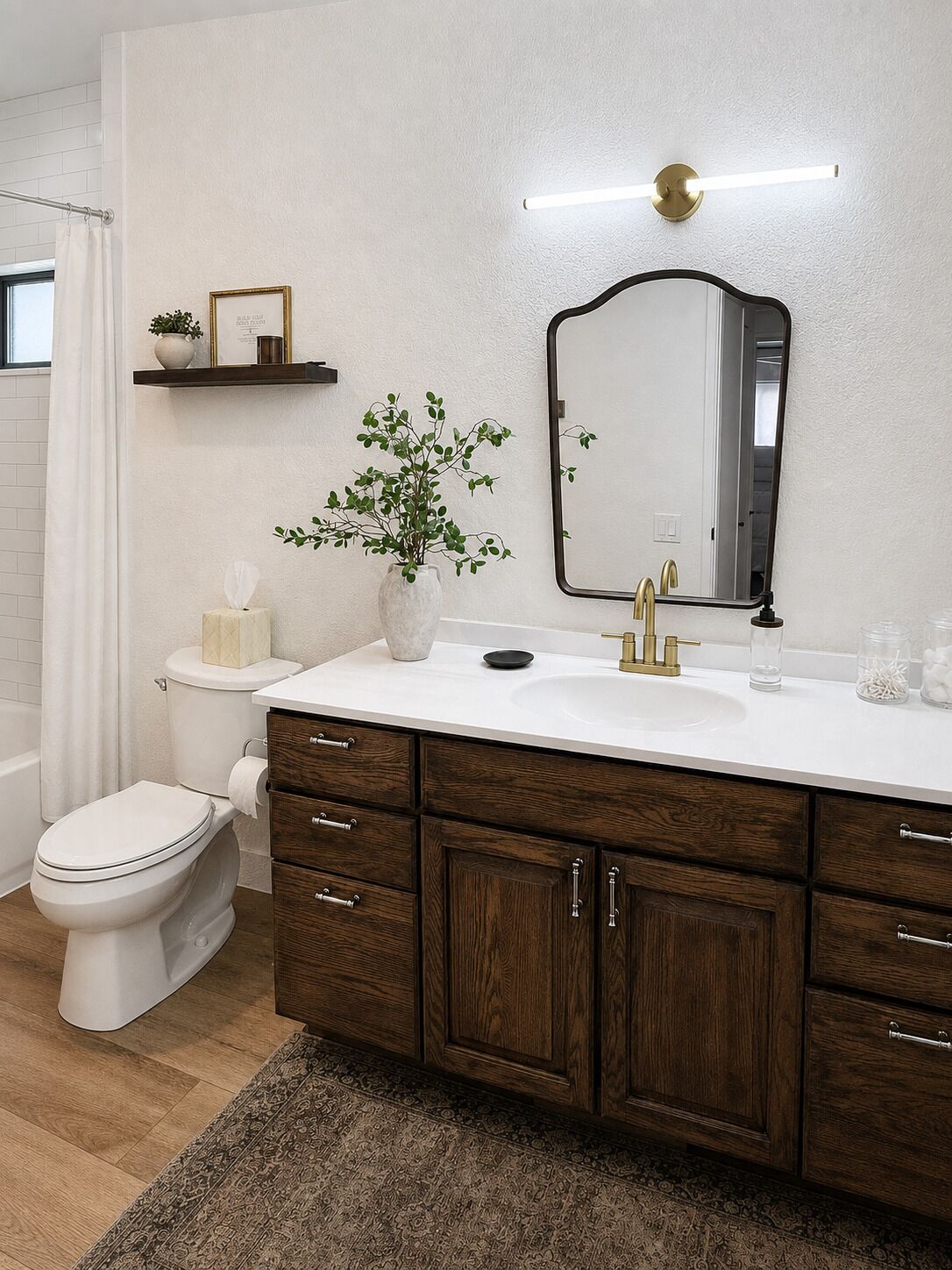 Un baño con inodoro blanco, tocador de madera con espejo y una pequeña estantería con objetos decorativos.