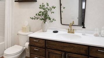 Un baño con inodoro blanco, tocador de madera con espejo y una pequeña estantería con objetos decorativos.