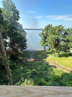 A lakeside view with a campfire, surrounded by trees and greenery.