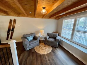 Relax in this inviting room with a high ceiling, two armchairs, and a woven rug.