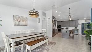 A modern kitchen with grey cabinets, a central island, and a dining area with a wooden table and white chairs. - Country Style Oasis! With cleared trails for walking or exploring (Polk City)