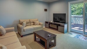A living room with a beige sofa, a coffee table, a flat-screen TV, and a sliding glass door leading to a balcony. - Charming Monroe Township Home - 13 Mi to RU! (Monroe Township)