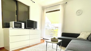 A modern living room with a flat-screen TV, a white cabinet, a grey sofa, and a small table. - Chic & central studio in the northern sunburns of Athens  (Agia Paraskevi)