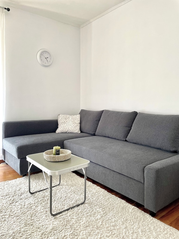 A modern living room with a grey sofa, a white rug, and a small table with a candle and a woven basket.
