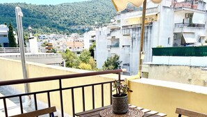 A balcony with two wooden chairs, a small table, and a potted plant. - Chic & central studio in the northern sunburns of Athens  (Agia Paraskevi)