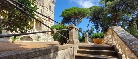 A stone staircase leading to a historic building with a tower, surrounded by trees and a clear sky.